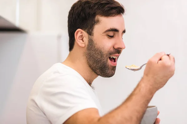 Photo of hungry young man eating breakfast from bowl. — Stock Photo, Image