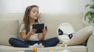 Sevimli, uzun saçlı bir kızın 4K yavaş çekim videosu makyaj için kozmetik fırça kullanıyor..