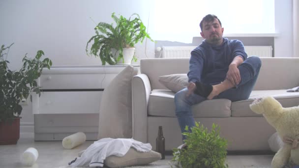 4k video donde el hombre después de beber alcohol huele su calcetín negro y luego seguir bebiendo en una habitación desordenada. — Vídeos de Stock