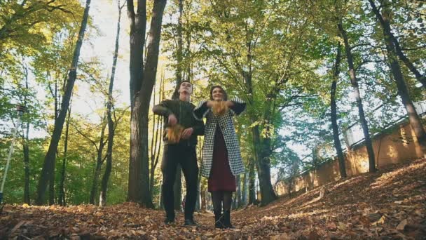 Una pareja está vomitando hojas de arce en el parque de otoño. 4K. — Vídeos de Stock