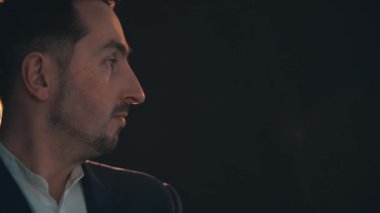 Ciddi genç yakışıklı adam ayakta duruyor, kameraya bakıyor, sonra yana bakıyor, biriyle konuşuyor..