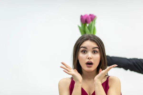 Une femme surprise reçoit un bouquet de fleurs de tulipes roses sur fond blanc. — Photo