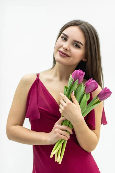 Cute girl with a bouquet of tulips looks with pleasure and smiles tenderly.