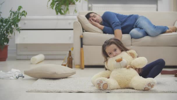 Filha brincando enquanto pai bêbado dormindo no sofá atrás em vídeo 4k. — Vídeo de Stock