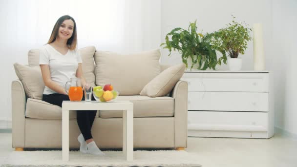 4k уповільнення відео вагітної жінки сидить на білому дивані . — стокове відео