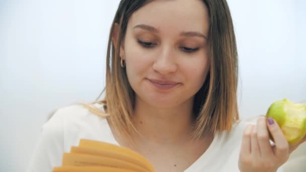 4k primer plano de cámara lenta de vídeo de la mujer embarazada con manzana leyendo un libro. — Vídeos de Stock