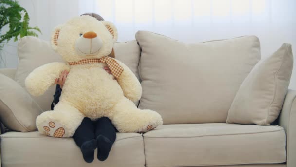 Pequena menina sorridente sentada no sofá com seu brinquedo ursinho de pelúcia em 4k slow motion vídeo. — Vídeo de Stock