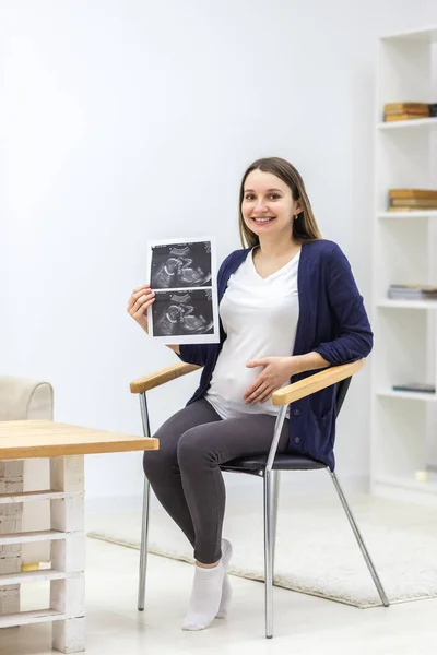 Foto einer schwangeren Frau, die auf dem Stuhl sitzt und einen Ultraschallbericht hält. — Stockfoto