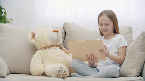 4k video de niña leyendo un libro a su osito de peluche. — Vídeos de Stock