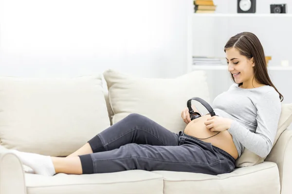 ヘッドフォンでソファの上に寝そべっている妊婦の写真. — ストック写真
