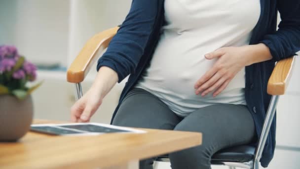 4k slow motion video de la mujer embarazada sentada en la silla mirando a su bebé en la foto. — Vídeo de stock