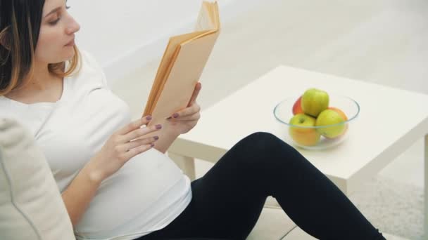 4k slowmotion video van zwangere vrouw het lezen van een boek en het aanraken van haar maag. — Stockvideo