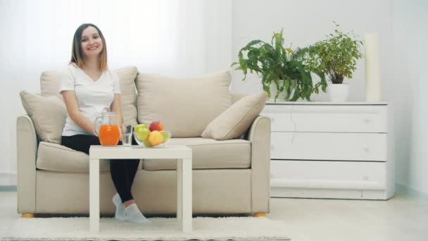 4k slowmotion видео беременной женщины, сидящей рядом со столом с фруктами и апельсиновым соком. — стоковое видео