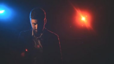 4K yavaş çekim videosunda takım elbiseli bir adam koyu arkaplanda mavi ve turuncu ışıklarla hava öpücüğü yolluyor..