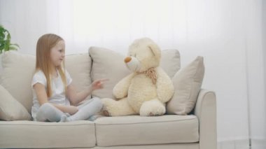 4K yavaş çekim videosu. Beyaz elbiseli küçük kız oyuncak ayıyla konuşuyor..