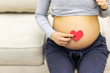 Hamile bir kadının kırmızı kalple karnının ve elinin kesilmiş fotoğrafı..