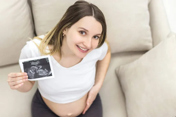 Foto von schwangerer Frau mit Ultraschallbericht zu Hause. — Stockfoto