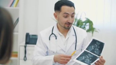 Doktorun beyaz önlük giyip ultrason fotoğraflarını tutarken ve açıklama yaparken 4K videosu..