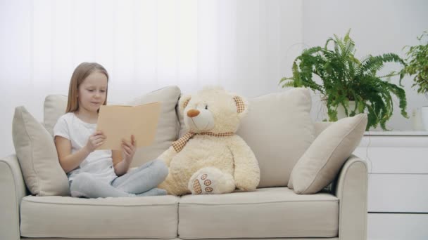 4k slow motion video de niña leyendo un libro a su osito de peluche. — Vídeos de Stock