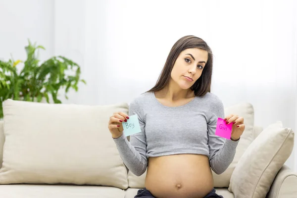 Photo de la femme enceinte tenant des papiers roses et bleus qui signifient le sexe du futur bébé. — Photo