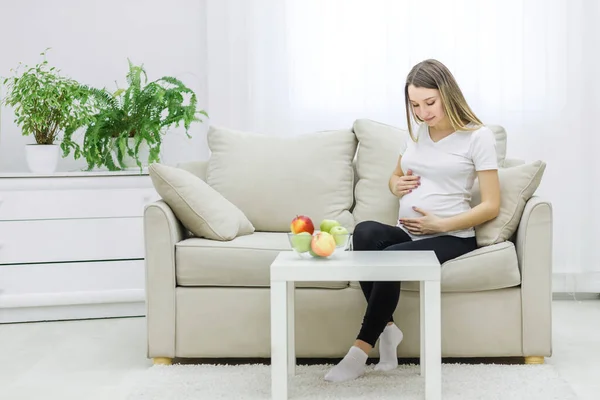 Foto einer jungen Frau, die ihren Bauch auf dem Sofa berührt. — Stockfoto