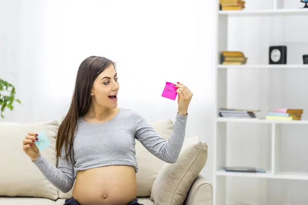 Photo de femme enceinte positive tenant des papiers roses et bleus qui signifient le sexe du futur bébé. — Photo