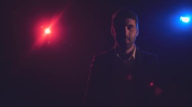 4K yavaş çekim videosunda takım elbiseli bir adam koyu arkaplanda mavi ve turuncu ışıklarla hava öpücüğü yolluyor..