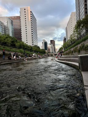 20 Kasım 2025, Kore - Alacakaranlıkta, yüksek şehir binaları ve yumuşak mavi gökyüzü ile çevrili nehir kenarındaki yaya geçidi. Kentsel yaşam tarzı ve modern şehir yaşamı temaları için ideal.