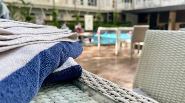 Düzgün istiflenmiş mavi ve beyaz çizgili havlular, sıcak bir sabah boyunca otelin yüzme havuzunun yanında dinlenmeye davet eden suyun yanında otururlar. Rahatlatıcı lüks tatil yeri atmosferi, yaz tatili, boş zaman, konukseverlik ve seyahat yaşam tarzı konsepti.