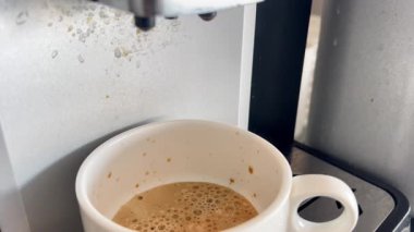 Profesyonel kahve makinesinin yakın plan görüntüleri beyaz bardakta sütlü kapuçino hazırlıyor.