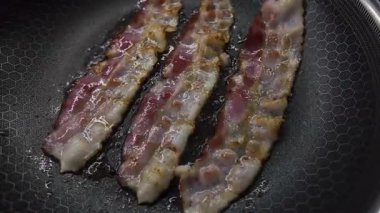 Kendi yağlarında pişen üç lezzetli domuz pastırmasının yakın çekimi. Koyu altıgen tavada pişirilmiş, sağlıklı ve geleneksel bir yemek için mükemmel.