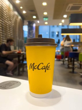 Poznan, Polonya - 11 Eylül 2025: McCafe sarı tek kullanımlık fincanı, koyu kapaklı, yoğun bir McDonald 's restoranında beyaz masada, elverişli fast-food kahvesini temsil ediyor.