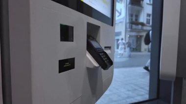 Umumi bir şarj istasyonuna akıllı telefon yerleştiren bir elin yakın plan görüntüsü, akıllı bağlantı için kırmızı bir tarama ışığı ve dijital ekran içerir