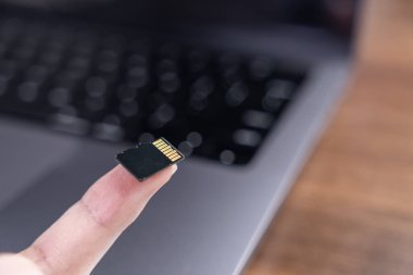 Bilgisayardaki hafıza genişlemesini ve bilgi yönetimini gösteren altın bağlantı iğneli küçük siyah bir mikroSD kartı dikkatlice gösteren bir parmak görüntüsü