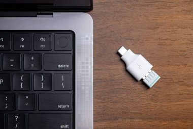 Çağdaş bir dizüstü bilgisayarın yanında, kusursuz veri alışverişi ve çevresel kullanım için çeşitli cihazları birbirine bağlayan ahşap bir masadaki USB-A adaptörü için temel beyaz USB-C
