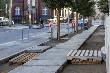 Kentsel kaldırımda açık toprak, yeni beton kesitler ve işlevsel ahşap paletler ile mevcut inşaat faaliyetleri gösterilerek, kentin yenilenmesi sırasında yaya akışının kolaylaştırılması