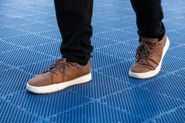 Göze çarpan parlak mavi desenli rendeleyici, modern moda ve şehir tarzını ön plana çıkaran, kahverengi dantelli ayakkabılar ve siyah pantolonlar giyen şık bir bireyin yakın çekimi.