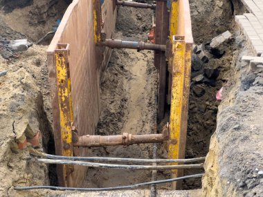 Karmaşık kamu işleri ve altyapı onarım operasyonları sırasında işçi güvenliği için hayati önem taşıyan sağlam metal destekleme ekipmanlarını gösteren güvenli bir inşaat siperinin içine bak