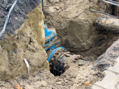 Kritik onarımlardan geçen mavi ve siyah borulara ve kablolara sahip derin bir siper, devam eden belediye altyapı gelişimi ve temel bakım hizmetlerini işaret ediyor