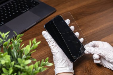 Profesyonel teknisyenin eldivenli elleri siyah bir akıllı telefondan kırık bir ekran koruyucusunu titizlikle çıkararak çok önemli mobil cihaz bakımı ve bakımı sunuyor.