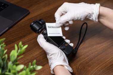 Poznan, Polonya - 16 Ekim 2025: DJI Osmo Pocket kamera, cihazı tutan beyaz koruyucu eldivenli bir kişi, videograflar ve yaratıcılar için düzgün bir ekran temizliği gösteriyor