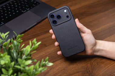 Poznan, Polonya - 16 Ekim 2025: Bir kişi bir iPhone 17 Pro 'yu elinde tutuyor, yerli PARIS' in siyah desenli çantasını ve kamera dizisini bir dizinin yanında sergiliyor