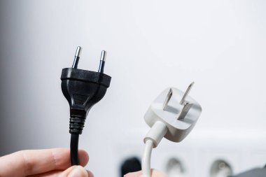 Küresel seyahat, güç farklılıkları, uluslararası adaptör gereksinimleri ve enerji çözümleri vurgulanan, beyaz üç toplu ABD dolgusu ile siyah Avrupa dolgusunu karşılaştıran ellerin yakın çekimi