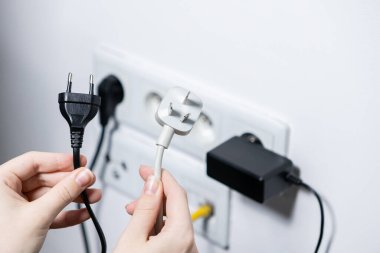 Bir kişinin elleri, evrensel seyahat adaptörleri ve bağlanabilirliğe duyulan ihtiyacı gösteren çoklu soket güç bandı yakınında Avrupa tip C ve İngiliz G elektrik prizlerini gösterir.