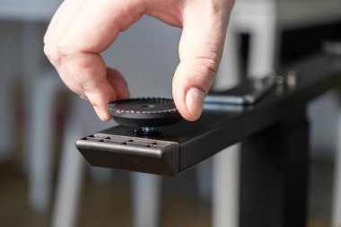 Koyu metal bir masa çerçevesinde ayağı düzleştiren siyah plastik bir el, ergonomik çalışma alanı için DIY montaj ve istikrarı vurguluyor