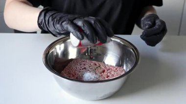 Şefin eldivenli ellerine yakından bak. Profesyonel bir mutfak ortamında lezzetli bir yemek için kırmızı biber, tuz ve biber gibi baharatlar serpiyor. Büyüt