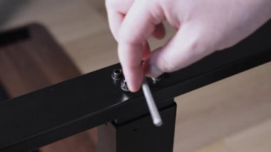 Siyah metal bir mobilya bacağının sürgüsünü sıkılaştırmak için Allen anahtarı çeviren birinin yakın çekimi dikkatli bir montaj ve ev bakımı anlamına gelir. Büyüt
