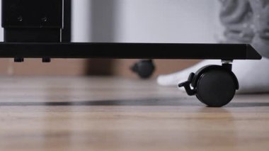 Doğal ahşap döşeme üzerindeki ergonomik mobilyalar için siyah bir caster tekerleğinin yakın görüntüsü, esnekliği ve evdeki adapte edilebilir çalışma alanı çözümlerini temsil ediyor