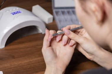 Kadın ellerinin, yapay tırnak uçlarına temiz jel sürerek manikür yaptığı yakın çekim görüntüsü, ayrıntılı bir ev güzelliği rutinini yansıtıyor.