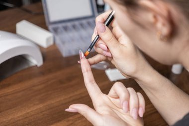 Evde uzun yapay tırnaklar yapan bir kadının ellerinin yakın plan çekimi. Profesyonel tırnak uzantıları için şeffaf bir jel sürerek şeffaf bir uç kullanıyor.